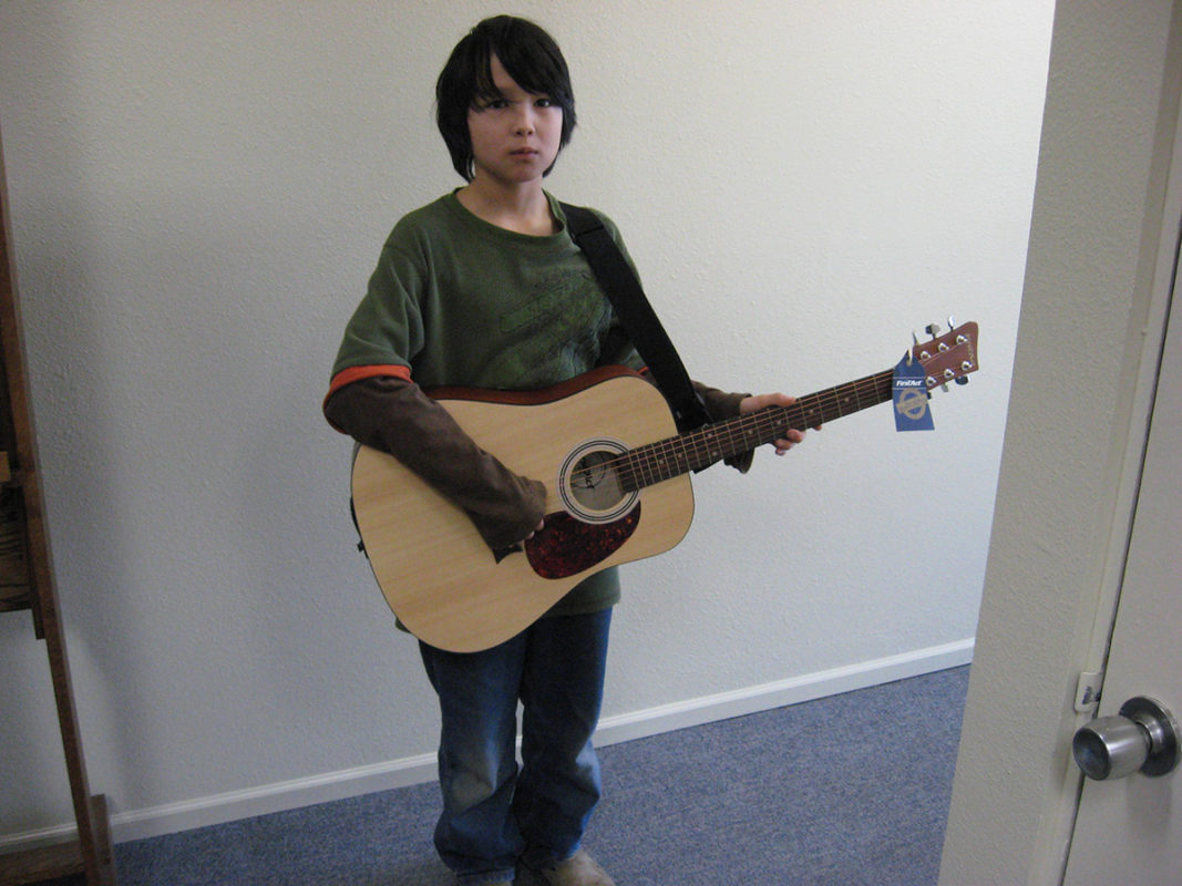Photo of a young boy holding an acoustic guitar.