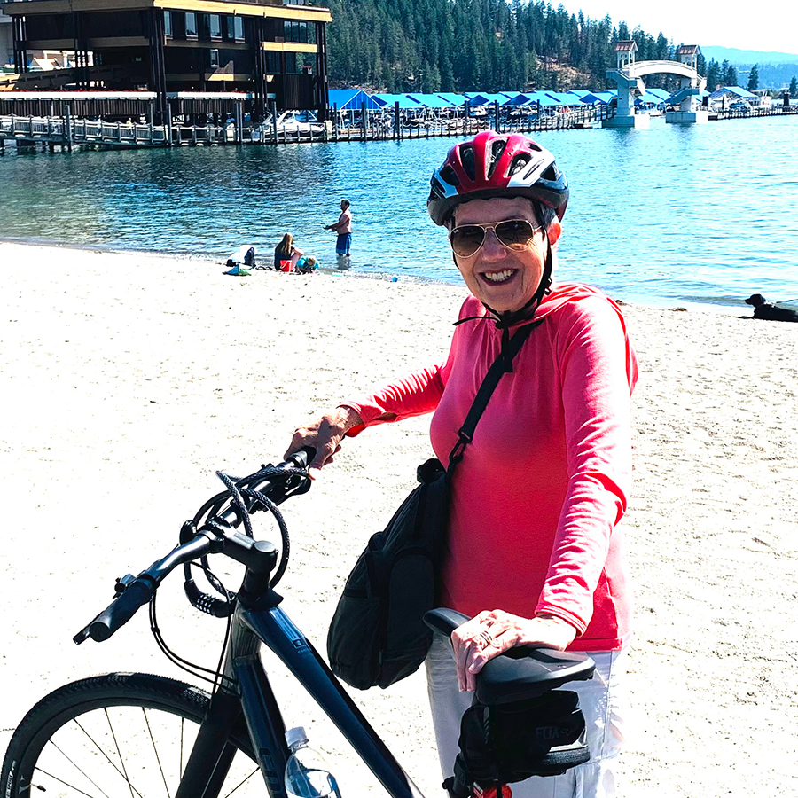 Photo of Diane Norman with a bike, bike helmet, and sunglasses in front of a lake.