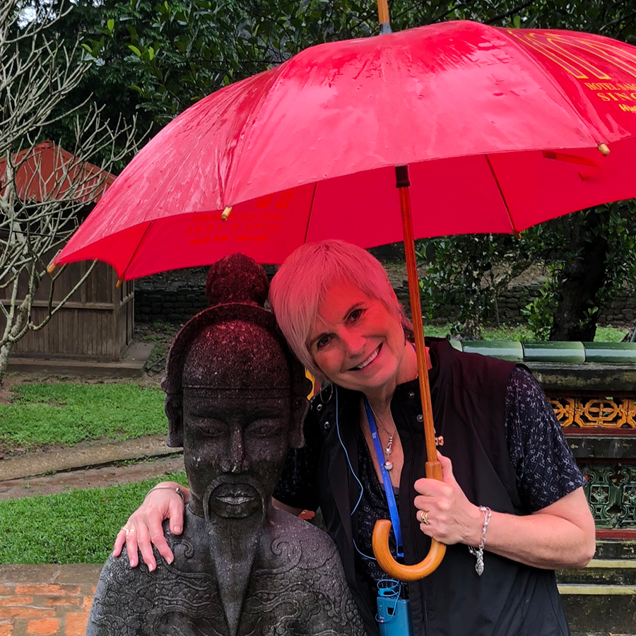 Photo of Karen Berry with a red umbrella and leaning on a statue of a person
