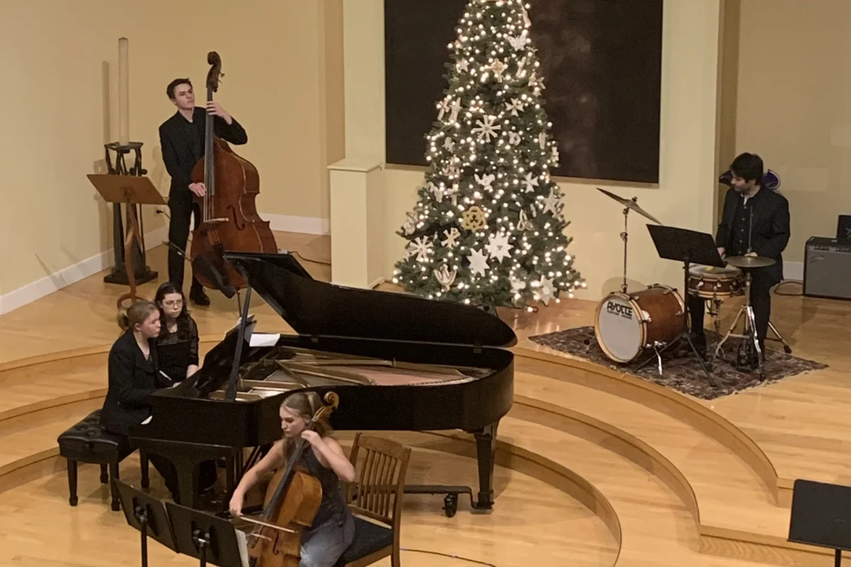 Wide overhead photo of musicians playing on a stage with a Christmas tree.