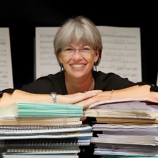 Photo of Board Member and Librarian, Ella Fredrickson, smiling an leaning on a stack of books.