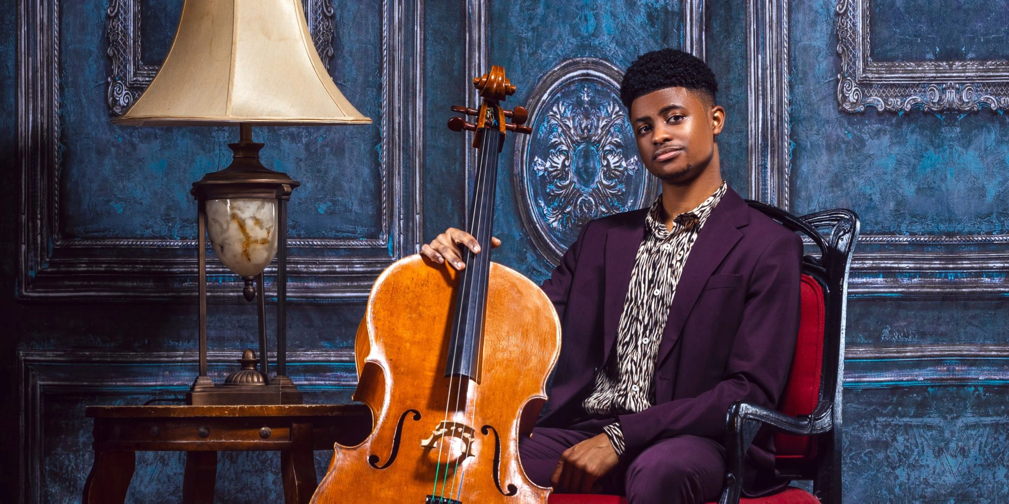 Portrait of Sterling Elliott, cellist, sitting in a chair holding a cello.