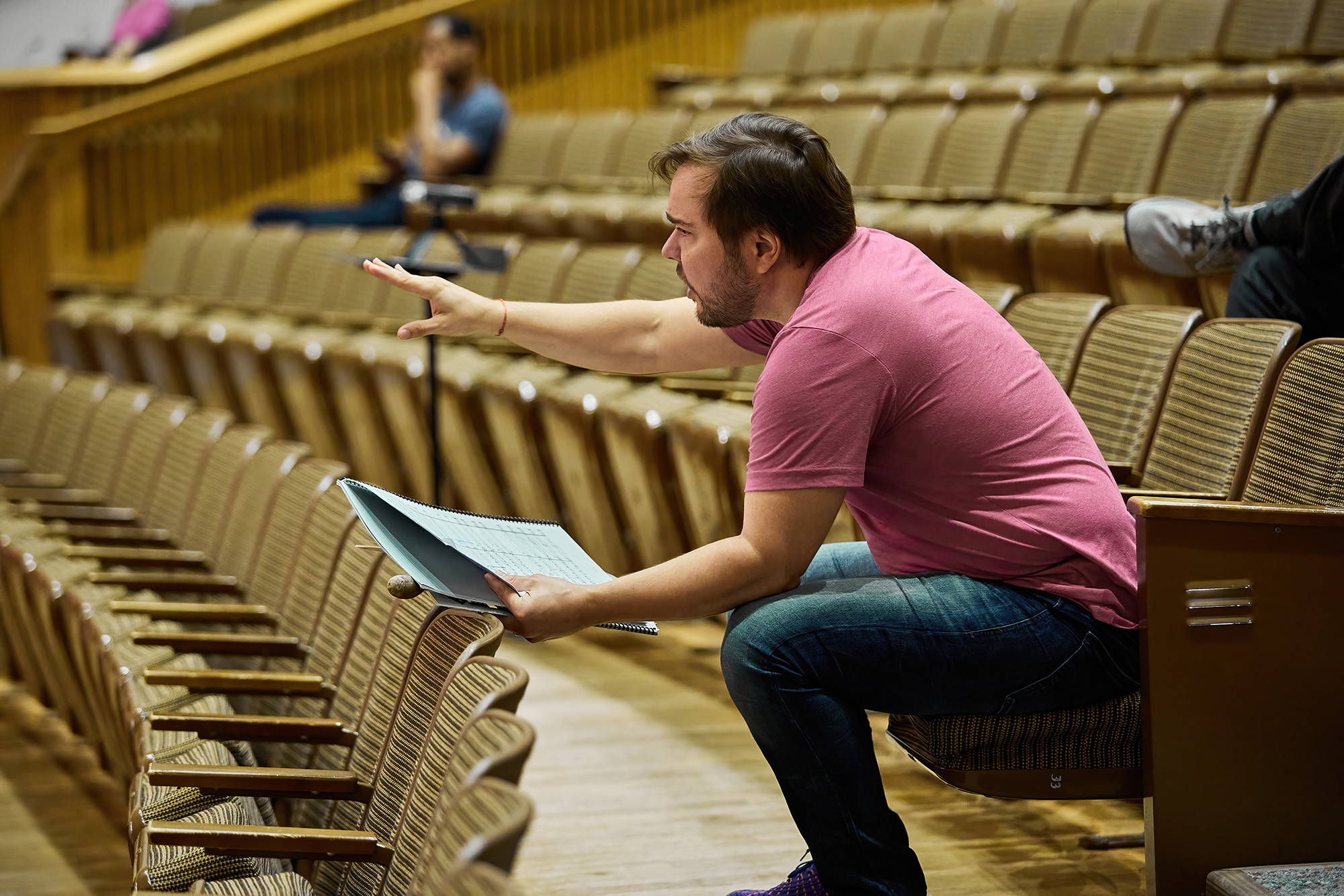 Marcelo Lehninger in rehearsal, seated in an auditorium with score in hand, giving expressive direction during orchestra practice.