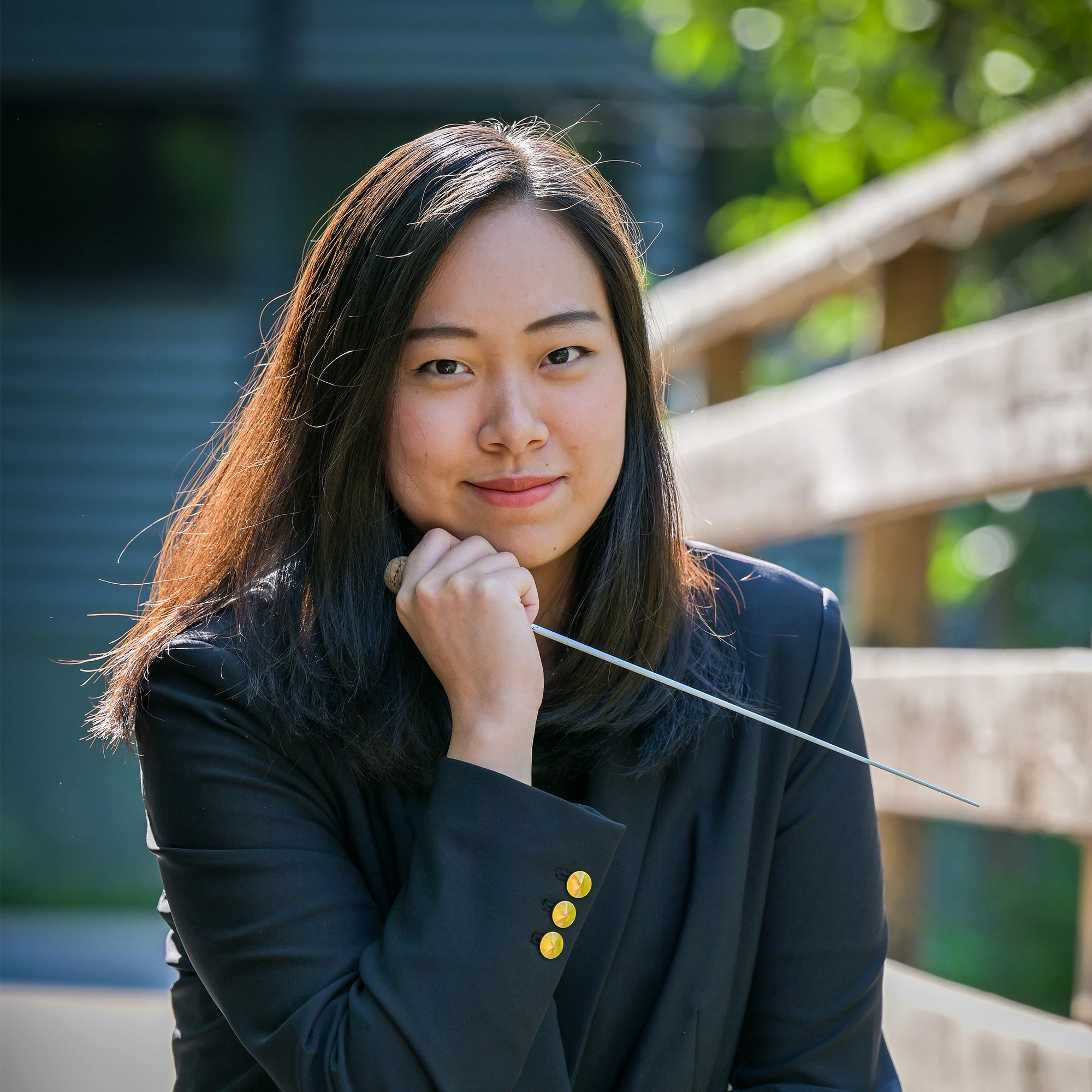 Portrait of Conducting Fellow Heidi Amanda Cahyadi, with the chin resting on her hand and holding a conducting baton.