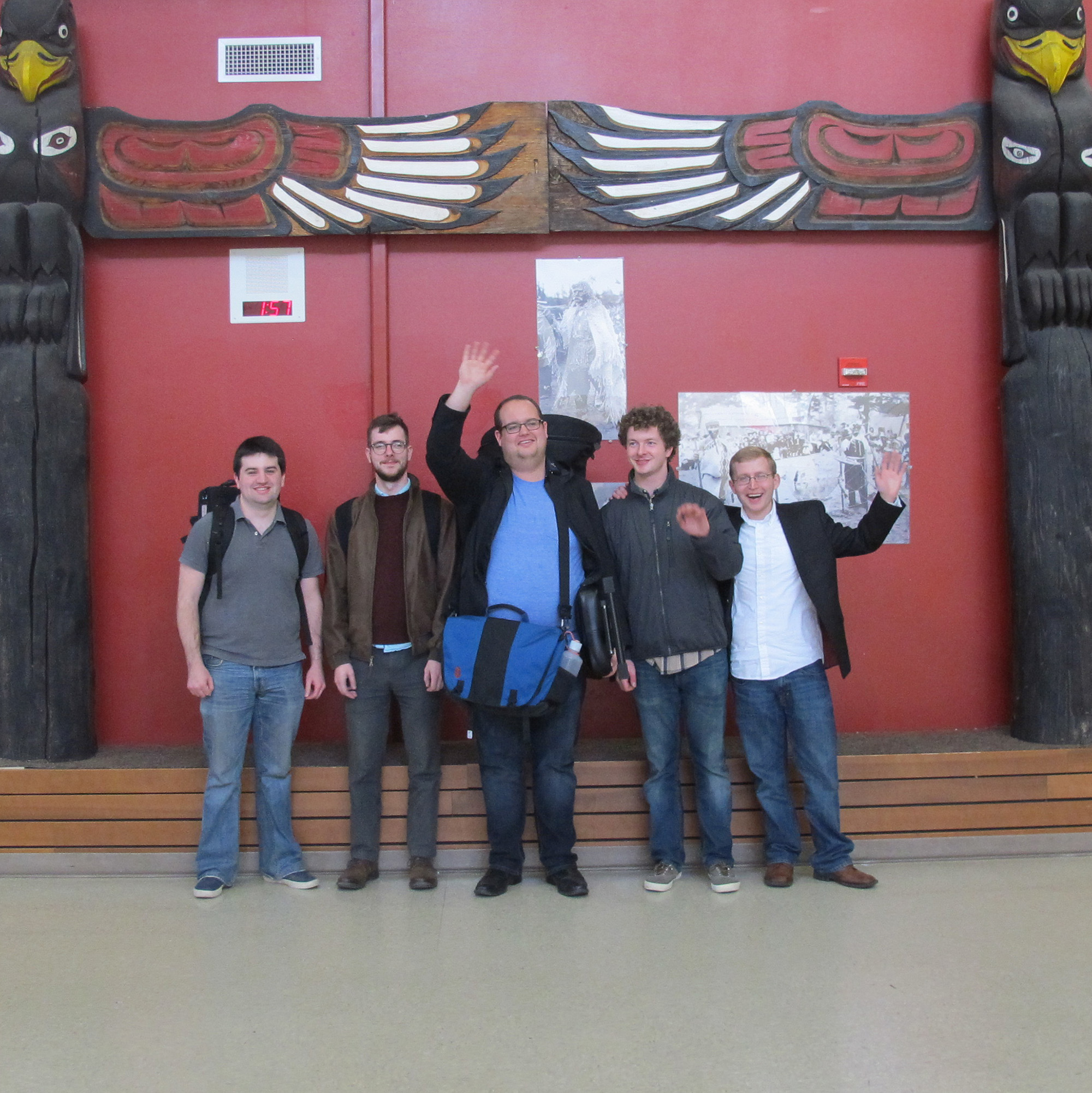 The 2nd Street Brass quintet standing together for a promotional photo in a venue decorated with traditional Northwest Coast carvings.