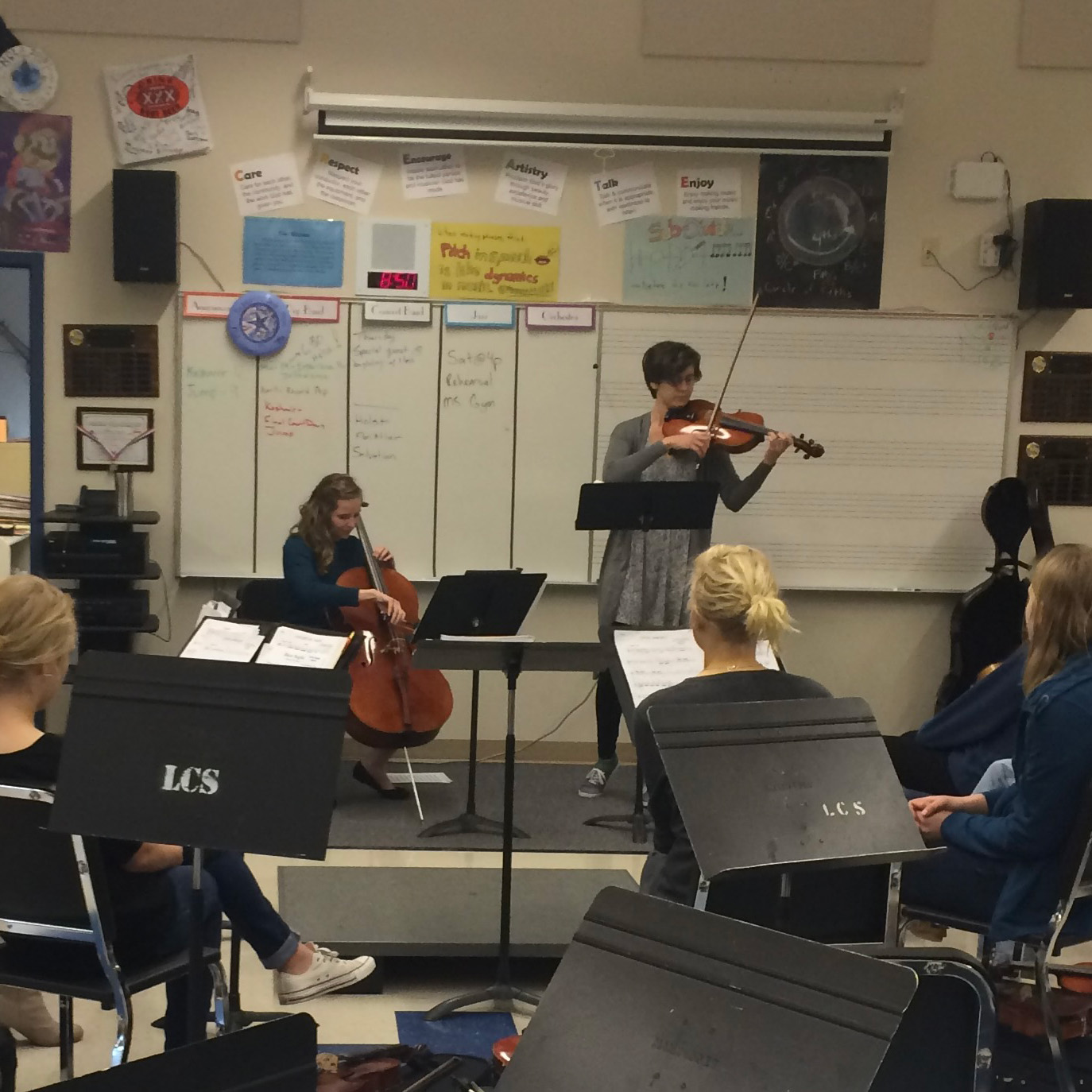 Musicians from the Colburn group performing an educational string duet for a student audience at a school.