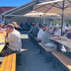 Patrons dining and socializing at outdoor picnic tables under patio umbrellas outside Stemma Brewing in Bellingham.