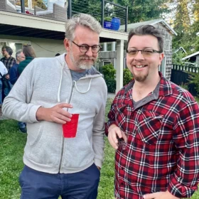 Justin and Allan chatting outdoors in Bellingham, Washington, holding drinks on a lawn during a summer gathering.