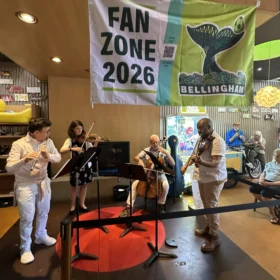 A chamber music ensemble performing under a Bellingham Fan Zone 2026 banner inside Mallard Ice Cream.