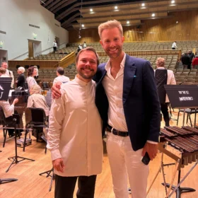 Marcelo and Andrew standing together and smiling on a concert hall stage next to a marimba during a WWU Music performance.