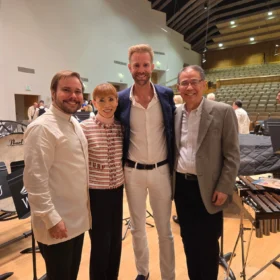 Marcelo, Andrew, Dave, and a colleague smiling together on stage at a WWU Music concert hall auditorium after a performance.