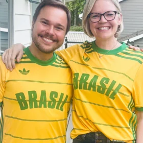 Marcelo and Erika smiling and posing together wearing matching yellow and green Adidas Brasil shirts on an outdoor deck.