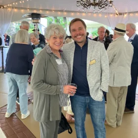 Carol and Marcelo smiling together under a lit tent at the Bellingham Festival of Music opening party.