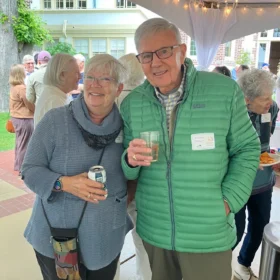 Ella and Andrew Moquin smiling and holding drinks under a lit tent at the Bellingham Festival of Music opening party.