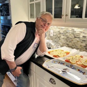 Charlie leaning against a kitchen counter next to platters of fresh salmon prepared with lemon slices.