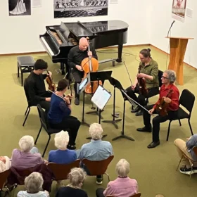 A classical chamber music ensemble performing with a piano and cello for a seated audience at the Whatcom Museum in Bellingham.