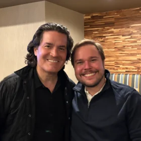 Zuill and Marcelo smiling together in a close-up indoor portrait.