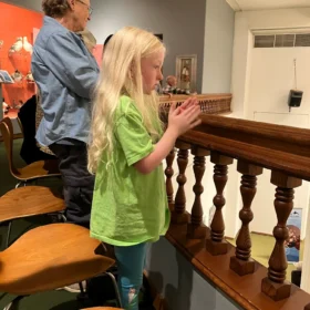A young blonde girl in a green shirt looking over a wooden balcony railing during an event at the Whatcom Museum in Bellingham.