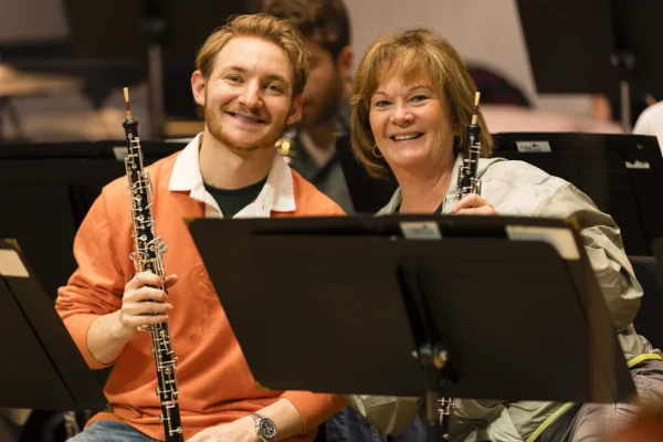 Two oboe players smiling and holding their instruments behind a music stand during a Bellingham Festival of Music rehearsal.