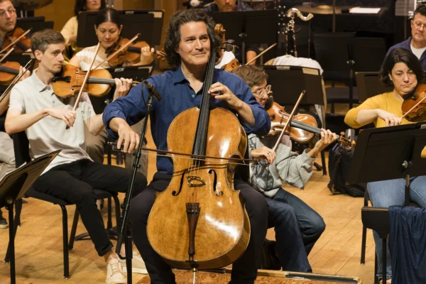Cellist Zuill Bailey performing a cello solo on stage backed by string orchestra musicians during a live concert.
