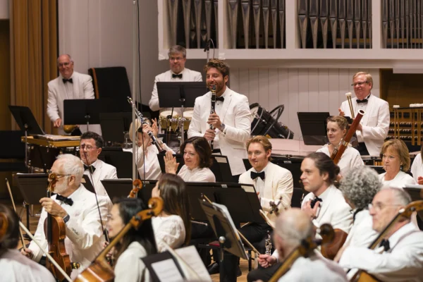 Featured clarinet soloist standing to acknowledge applause from the orchestra and audience on stage.