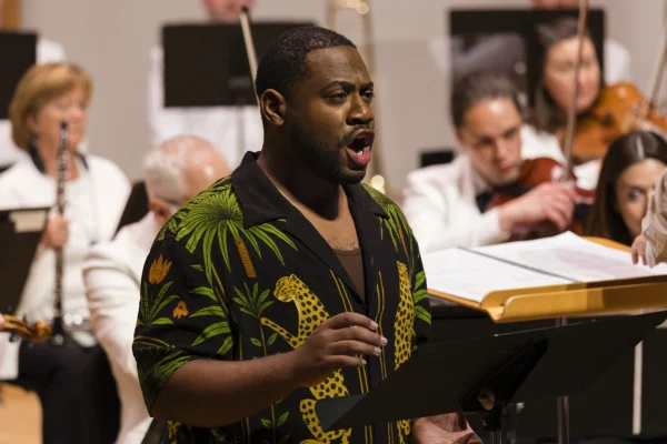 Baritone Key'Mon Murrah vocal soloist singing on stage accompanied by orchestra musicians during a live summer concert.