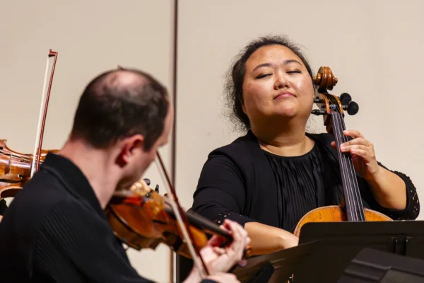 Close-up of a female cellist performing expressively with eyes closed alongside a violinist during a string ensemble concert.