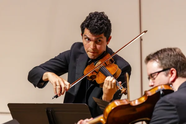Violinist playing intently with dynamic expression during a live string quartet performance on stage.