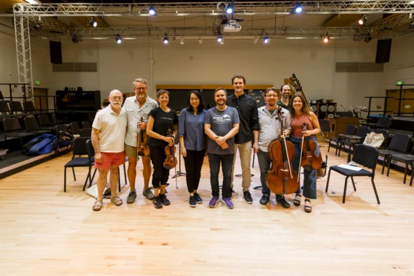Group portrait of conducting masterclass participants, instructors, and string musicians standing on stage together after a rehearsal.