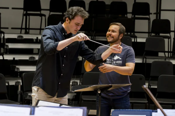 Instructor guiding a student conductor on baton technique during an interactive orchestral conducting seminar.