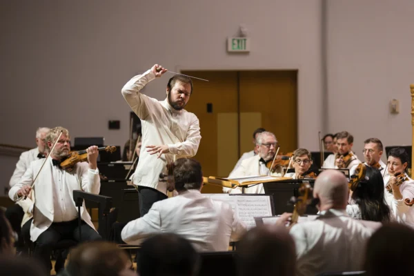 Expressive conductor Marcelo Lehninger raising a baton to direct the string section of an orchestra during a live concert.